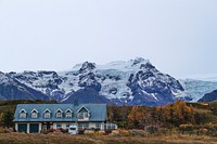 Cars parked in front of building with mountains in the background at Hótel Skaftafell. Original public domain image from <a href="https://commons.wikimedia.org/wiki/File:House_and_Mountain_(Unsplash).jpg" target="_blank" rel="noopener noreferrer nofollow">Wikimedia Commons</a>