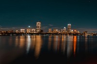 A bright skyline with a city waterfront seen from the water at night. Original public domain image from Wikimedia Commons