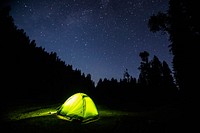 Light in a green tent surrounded by silhouettes of trees on a starry night. Original public domain image from Wikimedia Commons