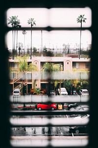 View through the window blinds on the parking lot, palm trees and two story residential building. Original public domain image from Wikimedia Commons