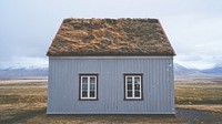 Snowflakes fall in front of a unique house with two windows and a grass roof in Iceland. Original public domain image from Wikimedia Commons