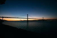 The end of a sunset behind a large suspension bridge over water in Lisbon.. Original public domain image from Wikimedia Commons