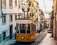 Yellow tram carriage suspended at the top of a narrow street with traditional architecture, Lisbon, Portugal. Original public domain image from Wikimedia Commons