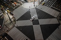 Drone view of crosswalk stripes in intersection in urban area with white car in the center. Original public domain image from Wikimedia Commons