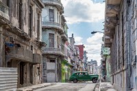 A vintage green car driving along dilapidated buildings. Original public domain image from Wikimedia Commons