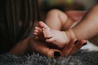 Infant's feet being held by a woman's hand with painted and manicured hands resting on a gray blanket. Original public domain image from Wikimedia Commons