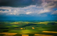 Wide shot of green and yellow agricultural fields with clouds overhead. Original public domain image from Wikimedia Commons