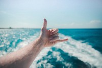 An outstretched hand making a “telephone” gesture over the white wake left in the sea by the boat. Original public domain image from <a href="https://commons.wikimedia.org/wiki/File:Hang_Loose_(Unsplash).jpg" target="_blank" rel="noopener noreferrer nofollow">Wikimedia Commons</a>