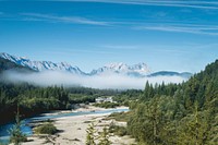 Sandy river banks surrounded by a misty forest with granite mountains on the horizon. Original public domain image from <a href="https://commons.wikimedia.org/wiki/File:Lost_in_the_Wilderness_(Unsplash_56pecHNfqIs).jpg" target="_blank" rel="noopener noreferrer nofollow">Wikimedia Commons</a>