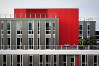 The exterior of a modern red and gray building with many windows and a checkered balcony. Original public domain image from Wikimedia Commons