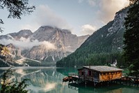 A log cabin lakehouse and dock on Lago di Braies with the snow-capped mountains in the background. Original public domain image from Wikimedia Commons