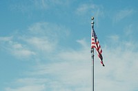 An American flag on a poll flying low against a blue sky. Original public domain image from Wikimedia Commons