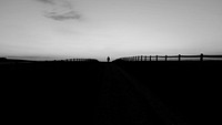 Black and white silhouette shot of person walking on horizon with wooden fence. Original public domain image from Wikimedia Commons