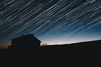 Long exposure photograph of the star trails above the silhouette of a house. Original public domain image from Wikimedia Commons