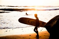 Surfer with a surfboard on a sand beach by the ocean at sunset in Carlsbad. Original public domain image from Wikimedia Commons