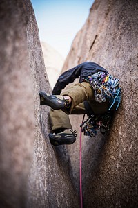 A rock climber scaling between two massive rocks and attached to a harness. Original public domain image from Wikimedia Commons