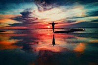 A man standing in the middle of beach with his reflection during sunset. Original public domain image from Wikimedia Commons