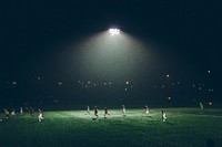 A soccer game being played at night under floodlights. Original public domain image from Wikimedia Commons