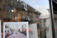 Vintage cameras and pictures hanging in window display with reflection. Original public domain image from Wikimedia Commons