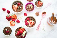 Cupcake filters and bowls filled with chocolate mixture, chocolate pieces, strawberries, raspberries, and daisies beside half dipped plastic spoons and a honey jar. Original public domain image from Wikimedia Commons