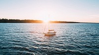 Sail boat on the ocean as sun rises above the forrest horizon. Original public domain image from Wikimedia Commons