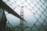 Aerial view from a chain link fence of the San Francisco golden gate bridge covered by fog. Original public domain image from <a href="https://commons.wikimedia.org/wiki/File:San_Francisco%27s_bridge_(Unsplash).jpg" target="_blank">Wikimedia Commons</a>