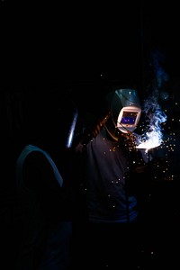 Two people weld in the dark in Nejapa. Original public domain image from <a href="https://commons.wikimedia.org/wiki/File:In_the_making_(Unsplash).jpg" target="_blank" rel="noopener noreferrer nofollow">Wikimedia Commons</a>