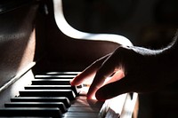 A person's hand playing the piano in the light. Original public domain image from Wikimedia Commons