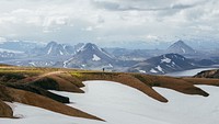 A person in the distance stands on a ridge and looks out at snowy mountains. Original public domain image from Wikimedia Commons