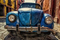 Front of a rusty, vintage, blue Volkswagen beetle on a cobblestone street, Blockbuster de San Miguel. Original public domain image from Wikimedia Commons