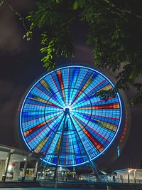 A bright and colorful ferris wheel spinning in circles in the middle of the night. Original public domain image from Wikimedia Commons