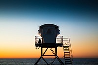 Silhouette of a man sitting alone against railing of a lifeguard tower, ocean and dusky sky in the background. Original public domain image from Wikimedia Commons