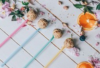 Rolled up balls of grain and oats on multicolored long plastic spoons beside sliced oranges, leaves, and flower petals on a white painted wooden deck. Original public domain image from <a href="https://commons.wikimedia.org/wiki/File:Energy_Balls_(Unsplash).jpg" target="_blank" rel="noopener noreferrer nofollow">Wikimedia Commons</a>