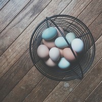 Eggs of different colors are placed in a basket on a wooden panel.. Original public domain image from Wikimedia Commons