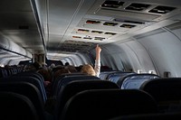 A child on a plane lifting their hand to adjust overhead controls above the seat. Original public domain image from Wikimedia Commons