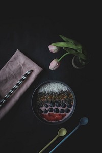 A flat lay shot of a fruit dessert, a vase of roses, spoons, straws, and napkin. Original public domain image from Wikimedia Commons