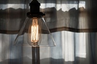 Hanging light in a clear lampshade with light tan curtains in the background. Original public domain image from Wikimedia Commons