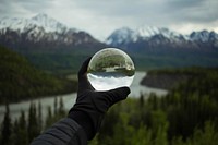 A person's hand in a glove holding a large glass ball against the backdrop of snowy mountains. Original public domain image from Wikimedia Commons