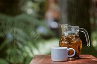 A pitcher of tea and a white mug on a wooden table. Original public domain image from Wikimedia Commons