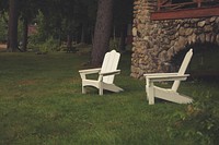 Two white lawn chairs beside a stone house next to a forest and picnic chairs. Original public domain image from Wikimedia Commons