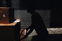 A silhouette of a person pushing a cart with cardboard boxes. Original public domain image from Wikimedia Commons