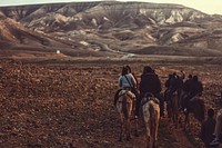 A group of people riding horses through dry wilderness towards a mountain range. Original public domain image from Wikimedia Commons