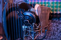 Professional studio headphones resting on a condenser microphone with a pop filter. Original public domain image from Wikimedia Commons