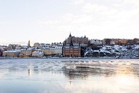 A Swedish city with tan and brown buildings by the shore of a frozen lake. Original public domain image from <a href="https://commons.wikimedia.org/wiki/File:Stockholm_(Unsplash).jpg" target="_blank" rel="noopener noreferrer nofollow">Wikimedia Commons</a>