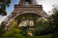 A close-up shot of the bottom of the Eiffel Tower with trees and water beneath it. Original public domain image from Wikimedia Commons