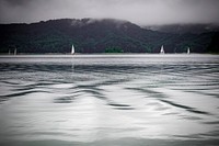 Sailboats line the coastline of grassy mountainside near calm waters. Original public domain image from Wikimedia Commons
