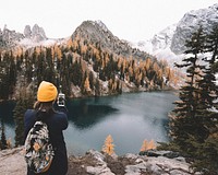 A person taking a photograph of the lake, mountains, and trees in North Cascades National Park. Original public domain image from Wikimedia Commons