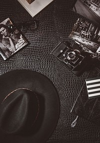 Vintage shot of hat, camera, glasses and monochrome photos lying on leather surface. Original public domain image from Wikimedia Commons