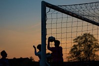 Three children play soccer at sunset at Ewen Fields. Original public domain image from <a href="https://commons.wikimedia.org/wiki/File:Silhouette_goalkeeper_catching_the_ball_(Unsplash).jpg" target="_blank" rel="noopener noreferrer nofollow">Wikimedia Commons</a>