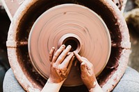 A person's hands crafting pottery on a spinning wheel. Original public domain image from Wikimedia Commons